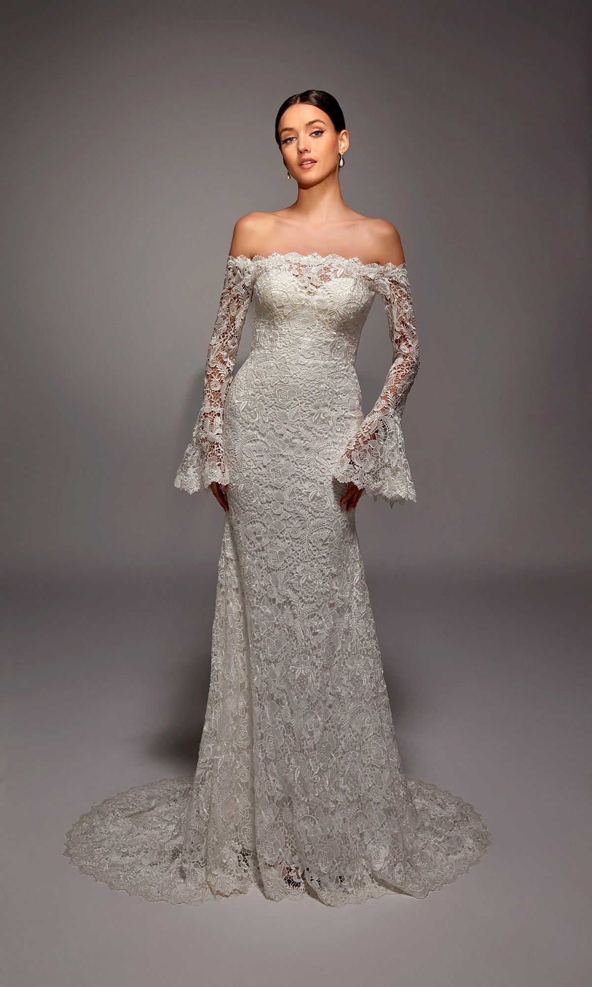 A woman wearing the Alyce 7156 long ivory dress stands in a studio with a neutral background.
